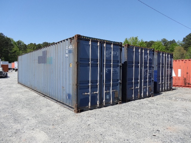 Two blue 40-foot cargo shipping containers in an outdoor yard, with clear sky and other containers in the background.