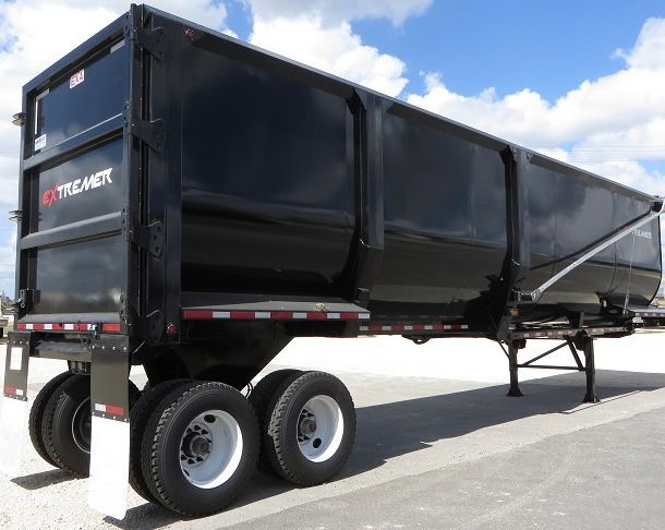 EXA scrap/demolition frameless dump trailer showing black body, tandem axles, and Extremer logo on rear.