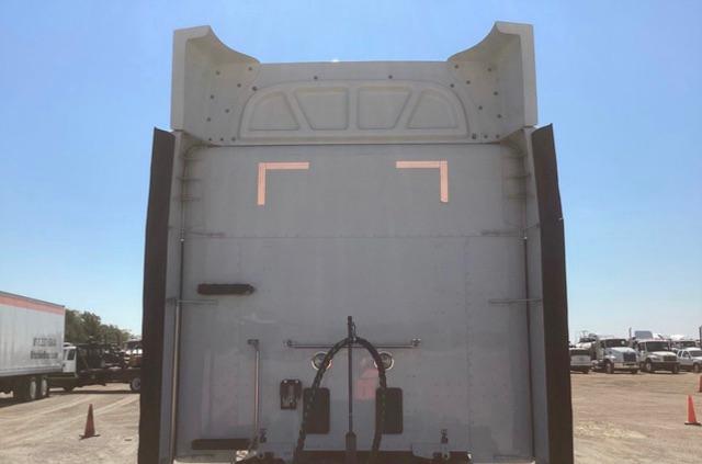 Peterbilt truck rear view showing trailer barrier and hitching mechanism, with light reflective markings and surrounding yard with other trucks.