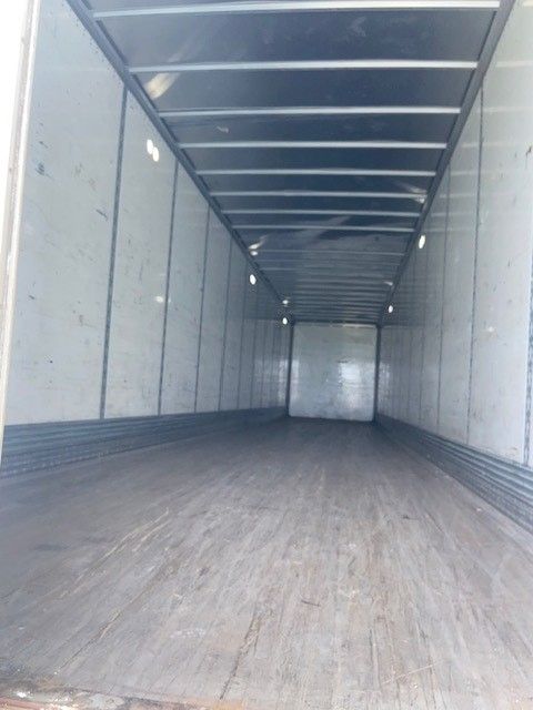 Interior of a long enclosed trailer with wooden floor and metal walls, overhead lighting, empty cargo space.