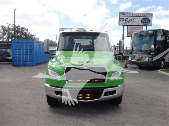 Front view of a green 2024 International MV tow truck with a chrome bumper and running lights, dealership lot in background.
