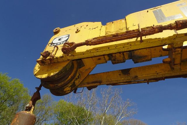 Grove RT58 crane arm with yellow paint and hydraulic cylinder, showing rails and hook assembly against a blue sky.