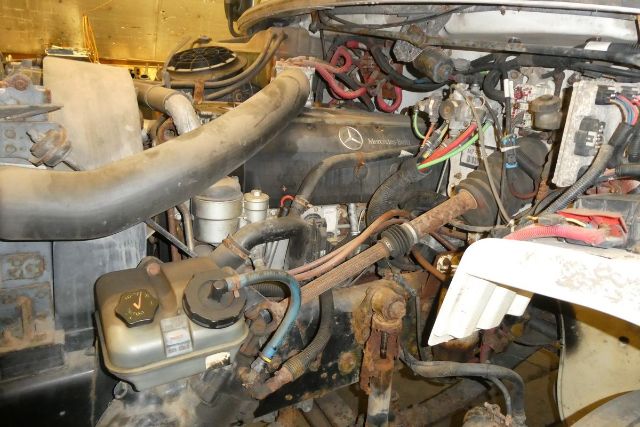 Box truck engine bay showing Mercedes-Benz engine components with hoses, wiring, and hydraulic lines.