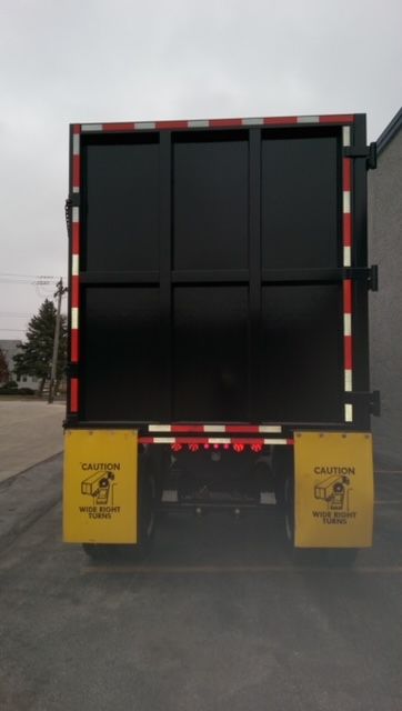Great Dane dump trailer rear view showing black round bottom hopper with caution panels and red-white reflective tape.