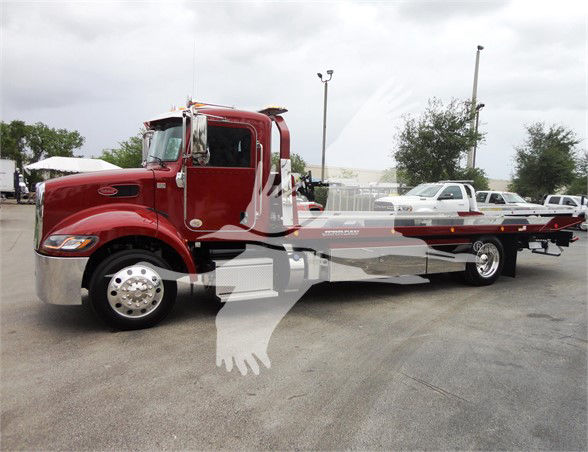Peterbilt 337 tow truck, red cab with flatbed, long wheelbase, chrome front bumper, large fuel tanks, daytime scene at a dealership lot.