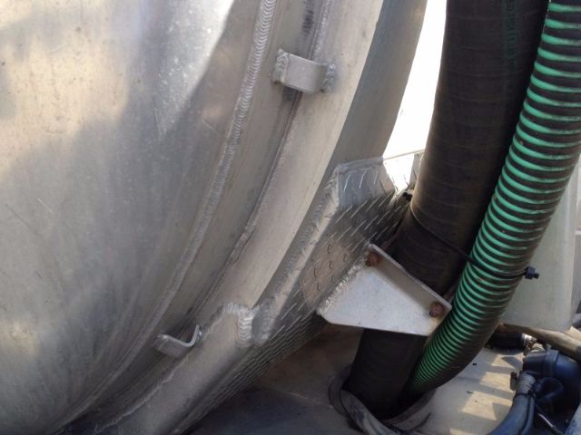 Vacuum tank truck side view showing metal tank, welding seams, a diamond-plate bracket, and green and black hoses.