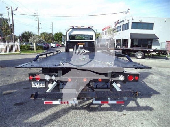 Freightliner flatbed tow truck rear view showing taillights, license plate DMR3765, and rear bumper with reflective stripes.