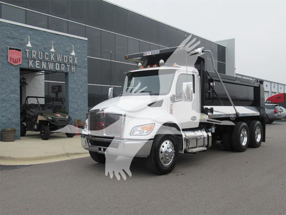 Kenworth T480 dump truck in white with black dump bed parked in front of a Kenworth dealership.