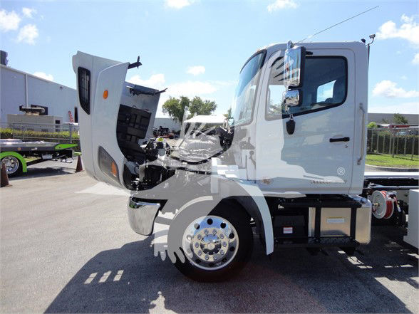 Front half of a 2022 Hino 268A tow truck with cab door open and hood raised, showing front wheel and engine area.