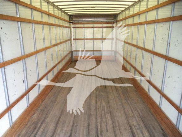Truck cargo box interior with wood floor and metal sidewalls; watermark of a running figure overlay. No visible labels, fluids, or part numbers discernible.