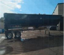 Trailer showing a steel frameless half-round dump with dual axles, black hopper, and tires. Text on image may include stock number and category; visible elements include trailer frame and crank, storage area, and sky.