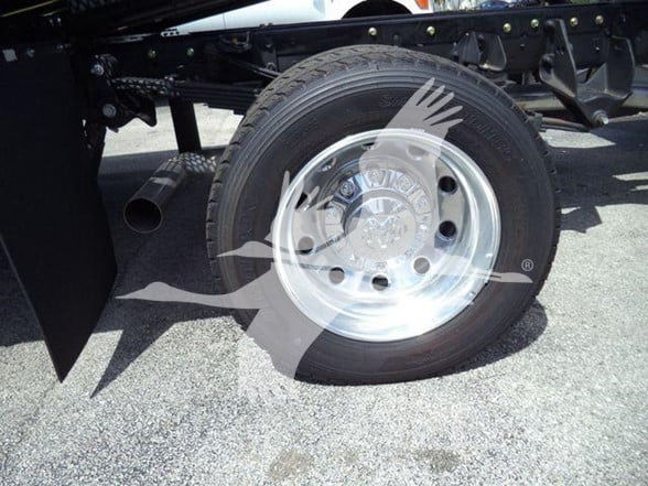 Truck wheel with chrome hubcap and tire, visible underbody framework and exhaust pipe.