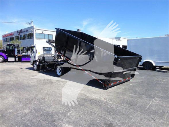 Isuzu NRR dump truck in a lot, hydraulic lifting bed raised on a trailer with a blue sky.