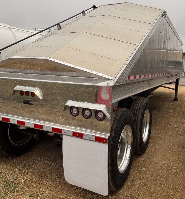 Aluminum sand/grain hopper trailer with polished metal diamond plate sides and triple rear lights. Dual rear wheels, white fender, reflective red/white tape, open-top hopper with riveted panels.