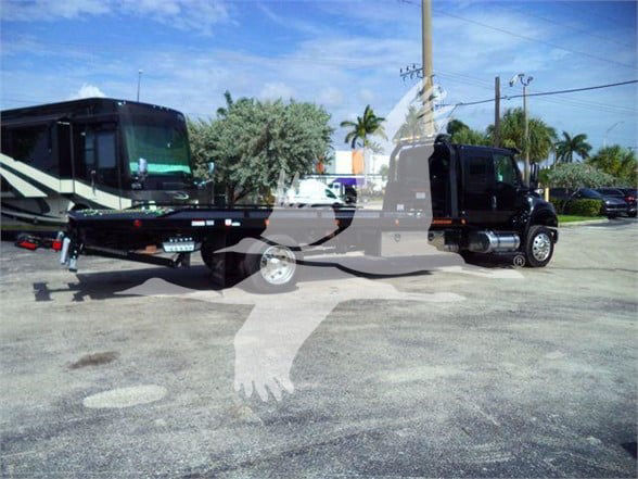 Tow truck with a flatbed trailer connected to a black International MV cab; watermark of a handshake graphic across the image.