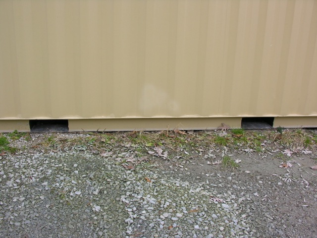 Container trailer side with small gaps at the bottom near the ground showing exposed blocks underneath.