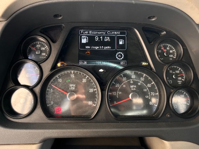 Peterbilt 579 dashboard showing instrument cluster and central display with fuel economy reading. Gauges include RPM x100, speedometer, and coolant/engine gauges. Center screen displays Fuel Economy: Current 9.1 MPG and Idle Usage 0.5 gal/h