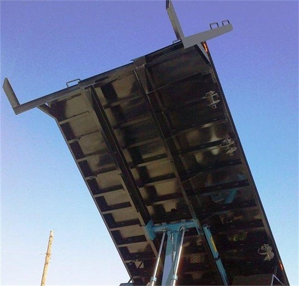 Flatbed truck body underside with hydraulic lift supports and latching mechanisms visible; blue hydraulic components near center; black metal bed panels and side brackets.