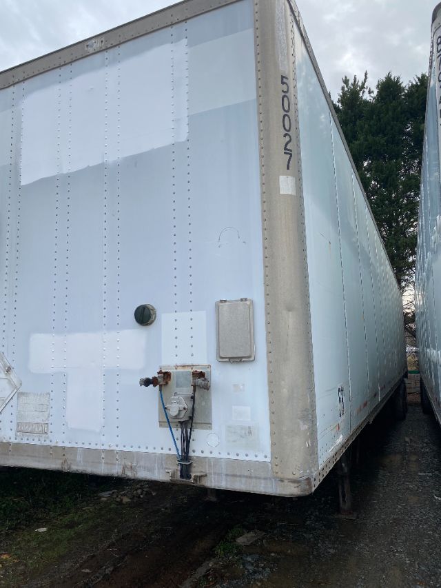 Trailer side and rear corner showing a light blue Duraplate Wabash trailer with riveted body, vertical corner post with identifying numbers, and a side-mounted electrical/hose connection panel.