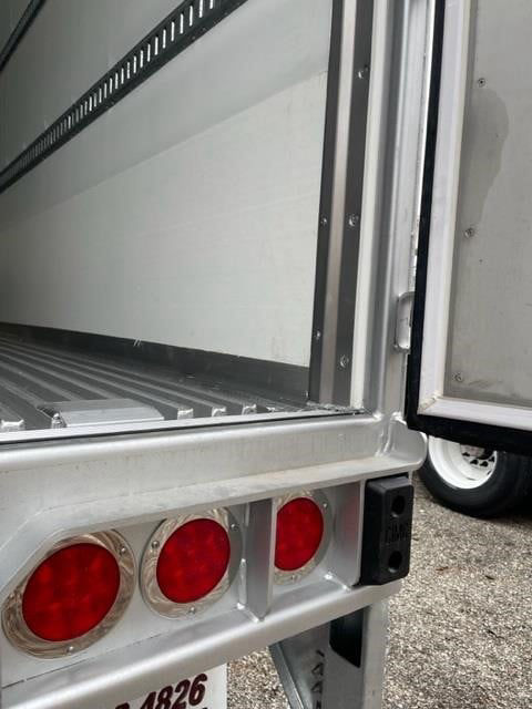 Rear corner of a CIMC cold storage trailer showing triple red rear lights and hinge area with a white interior wall; metal frame and open door.