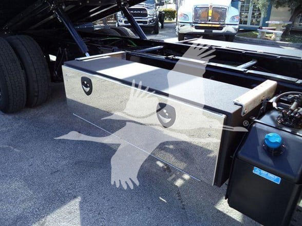 Truck bed toolbox and auxiliary fuel tank mounting under a semi-truck chassis with blue cap on reservoir visible.