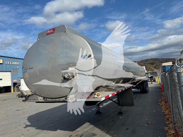 Tank trailer with a rounded cylindrical tank and pump off-line system, mounted on a long flatbed trailer, side view in a lot.