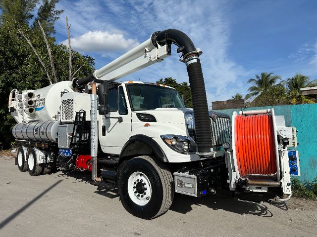 2013 International 7500 vacuum truck with large white cab, black exhaust hose, and red reel at the front right; side tanks and machinery along the chassis.