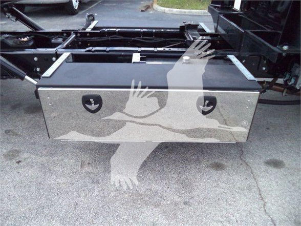 Front of a truck toolbox mounted under the chassis with two circular access doors and a textured metal surface, part of a 2023 International CV tow truck.