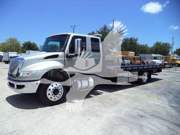 Tow truck with a silver International MV cab and flatbed, showing chrome front grille, dual exhaust, and large wheels. No visible branding text legible on the image.