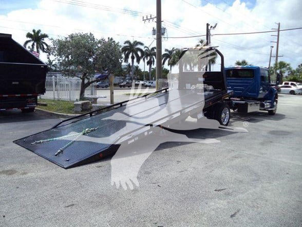 Tow truck with a long flatbed ramp in a parking lot. No visible labels legible on the vehicle in this image.