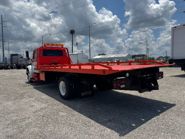 Tow truck with bright red flatbed and white cab, International 4700 DT 466E, rear view showing flatbed and hitch accessories.