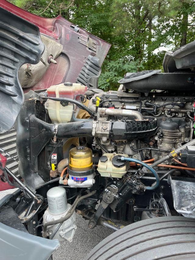 Freightliner Cascadia engine bay showing coolant reservoir, yellow oil filter, wiring, hoses, and various engine components.