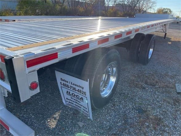 Flatbed trailer with aluminum deck and tandem axles, reflective red/white safety tape along sides, Fontaine REVOLUTION 52 53FT aluminum trailer. Stock number 561775.