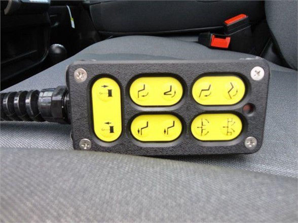 Panel with six yellow indicator buttons and a drive connector on left mounted on a vehicle seat, with symbols indicating hydraulic or seat controls.