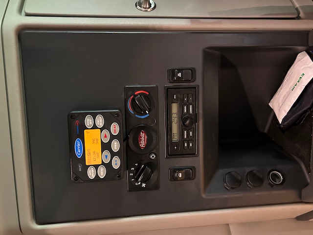 Peterbilt truck dash cluster with Carrier auxiliary gauge, climate controls, radio, and storage pocket.