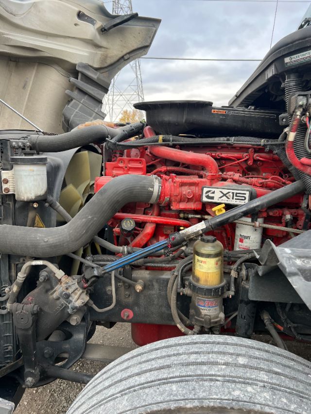 Truck engine bay of 2019 International LT625 showing red engine with X15 badge, large black intake hose, yellow oil filter, and front chassis components.