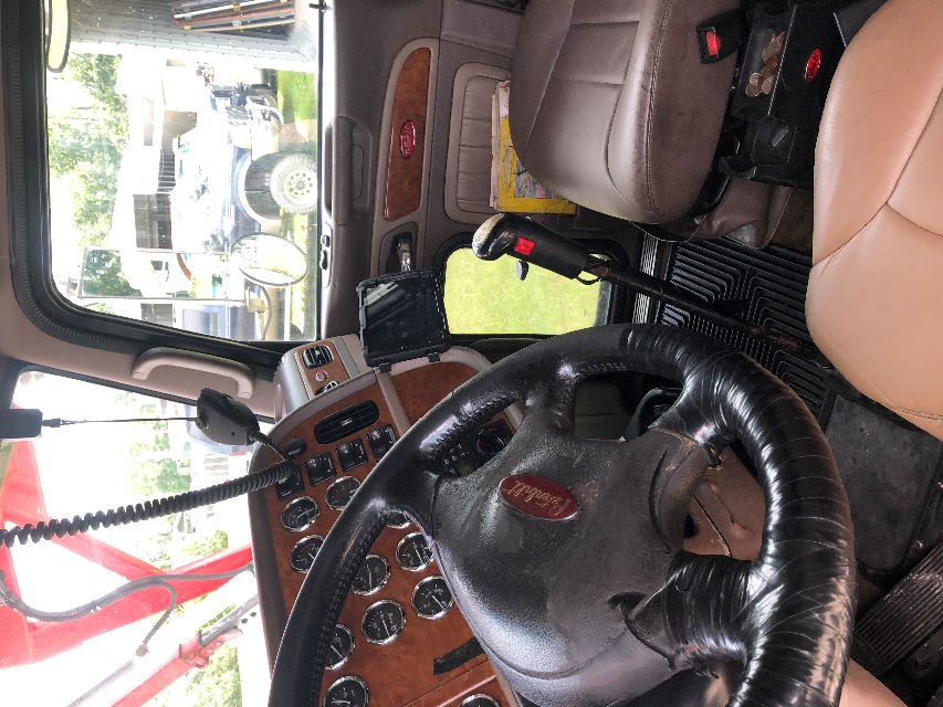 Peterbilt truck interior dashboard and steering wheel with wood grain accents, tan seats, and gear shifter visible.
