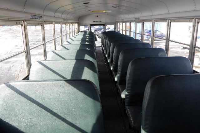 Interior of a used 2002 Freightliner FS65 bus showing rows of green upholstered seats along a central aisle and windows along both sides.