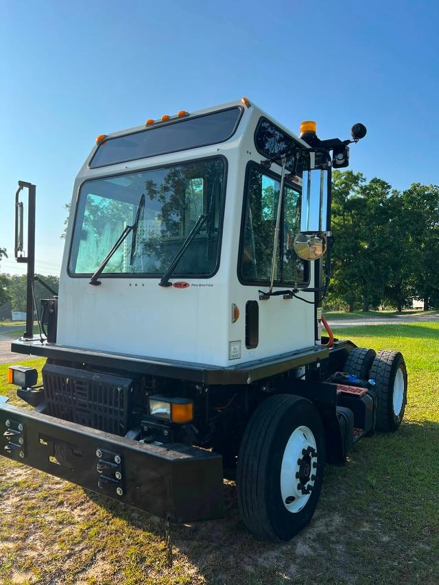 A white cab-over truck tractor in a yard, front and side view, with black bumper, dual rear axles, and white wheels.