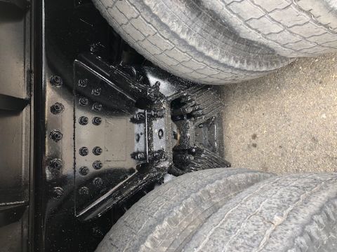 View under a Peterbilt 388 truck showing the chassis crossmember and dual rear axles with leaf springs.