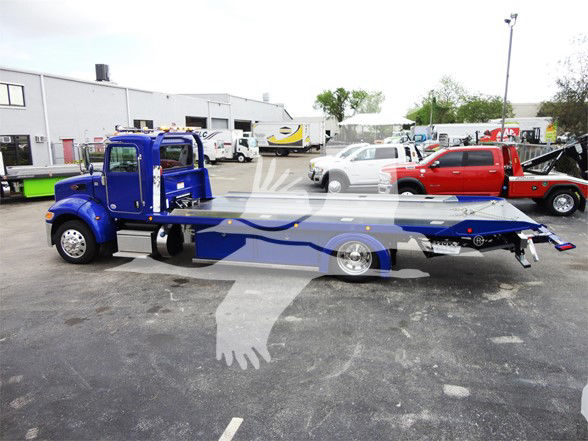 Blue Peterbilt tow truck chassis and flatbed with extended long wheelbase, cab at left, flatbed with winch and wheel at far right.