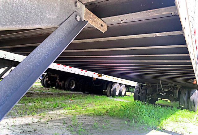 Underneath view of a Vanguard VXP trailer showing tandem axles and undercarriage with grass on ground.