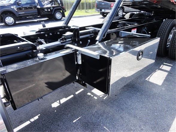 Kenworth W990 truck chassis with black toolbox/compartments mounted under the frame, hydraulic hoist legs, and attached hardware.