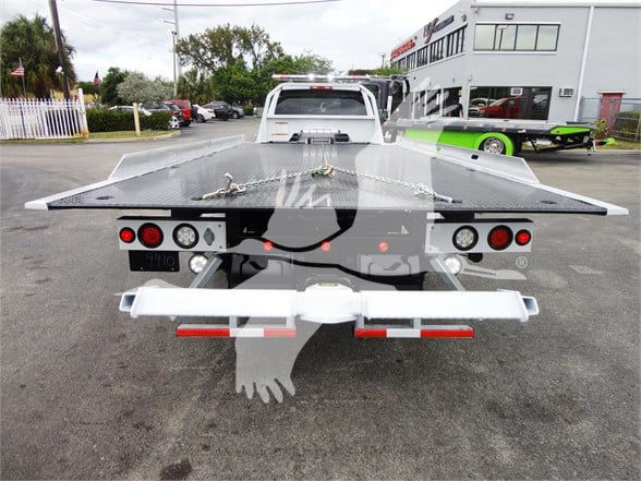 Ram 5500 tow truck bed seen from rear with flatbed and wheel ramps, rear lights visible, light bar, and hitch.