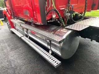 Truck side view showing fuel tank and aluminum side steps under the cab of a red 2023 Western Star 4900 conventional sleeper.
