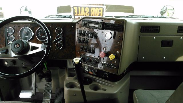 Interior of a 2007 International 9900i truck cab with steering wheel, dashboard, and gear shifter. Dash contains multiple gauges and a metal plate with switches and knobs.