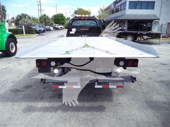 Tow truck bed with flatbed and rear lights visible; truck in background at dealership lot.