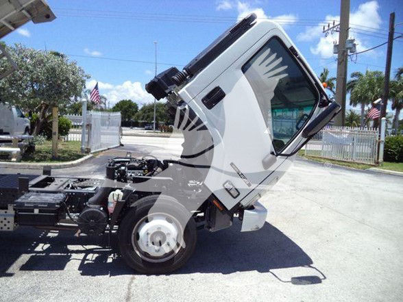 Isuzu NQR truck cab tilted upward in a lot showing chassis and front wheel.