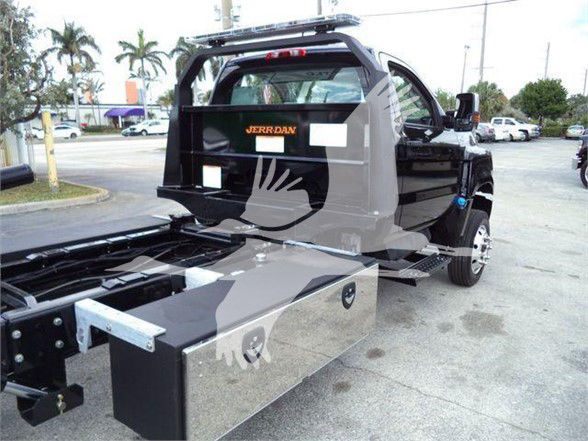 Truck bed view of a 2023 International CV tow truck with a large metal toolbox and rear rack, black cab, and chrome wheels.