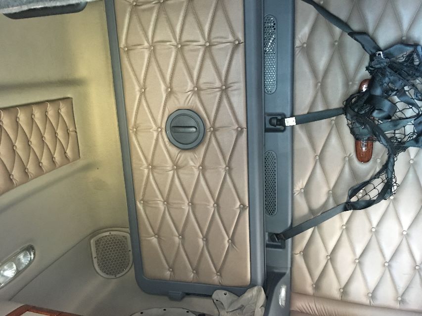 Truck cab interior ceiling with quilted tan headliner and storage hatch; visible circular ceiling vent and padded wall panels.